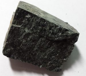 A dark, rough-textured mineral with two sets of straight cleavage marks separate by a jagged slice.