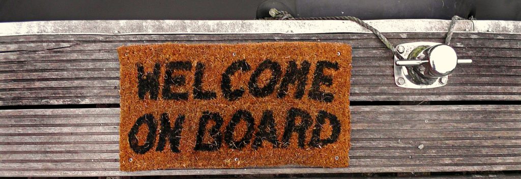Photograph of a welcome mat on a ship dock. The mat reads 