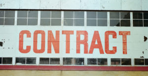 Photo of the side of an old brick building with a large white sign that reads CONTRACT in orange letters