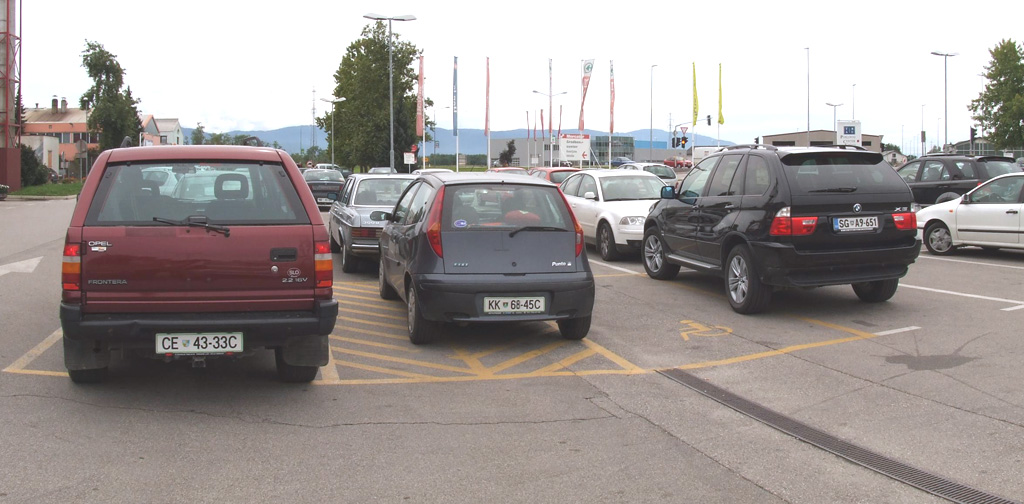 Photo of a parking lot, showing one car parked in a forbidden space; another car occupies two spaces (one is a handicapped-parking space)