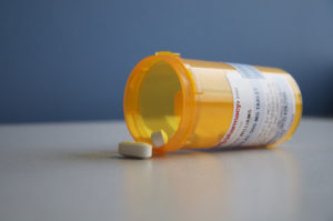 Photo of a pill bottle lying on its side with several white tablets spilling out.