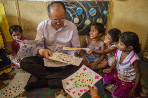 World Bank Group president Jim Yong Kim visits an integrated child development services and skills center in Delhi, India. He is shown sitting on the floor with a group of young children who show him their drawings.