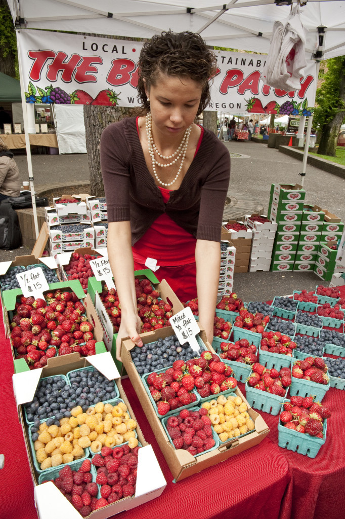 A woman adjusts baskets of berries at a stand in a farmer's market.