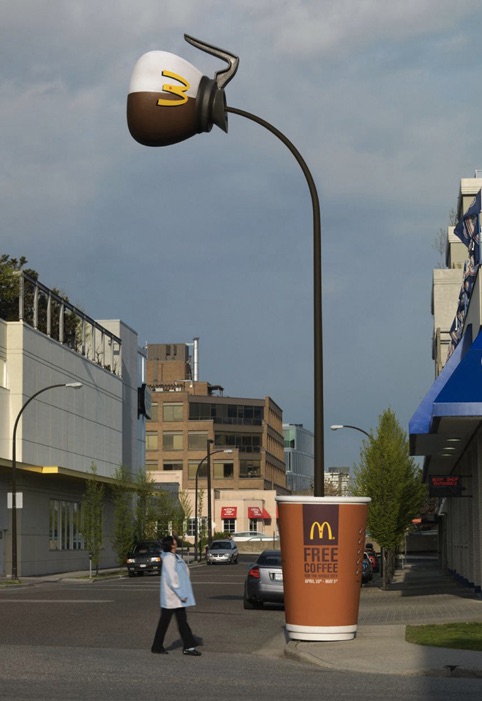 A man walks by an odd lamppost. The bulb of the light looks like a McDonald's coffeepot, while the base of the lamp looks like a McDonald's coffee cup. The pole of the lamppost looks like coffee being poured from the coffeepot into the cup.