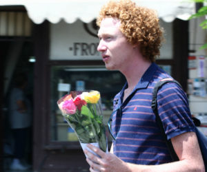 Photo of a worried-looking young guy carrying a small bouquet of roses.