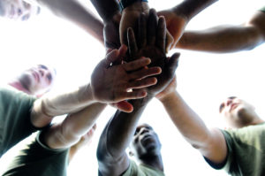 Photo of a team huddle; members each place a hand in the center atop another member's hand.