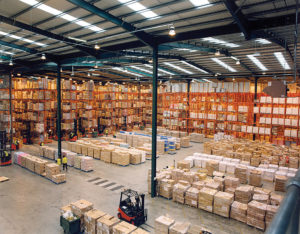 Photo of a giant warehouse with pallets loaded with goods and forklifts.