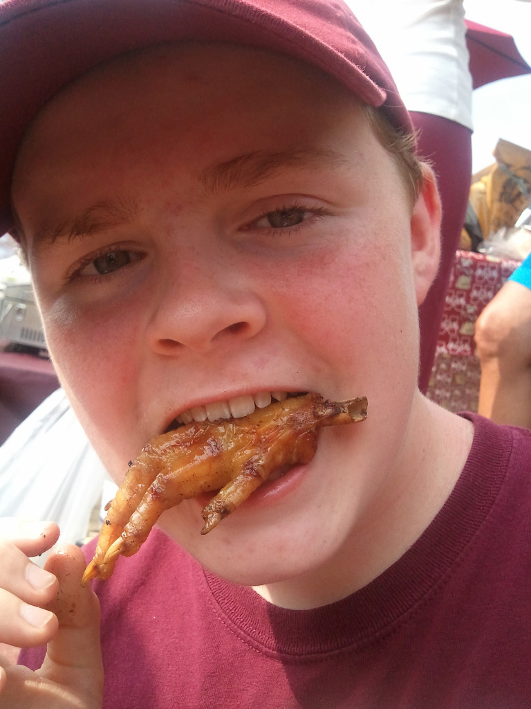 Photo of a boy with a fried chicken foot in his mouth.