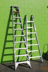 Photo of two ladders leaning against a green wall.