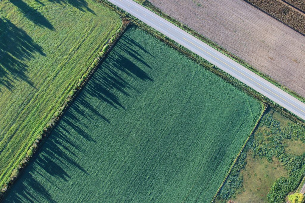 An aerial photograph of three large fields by a road.