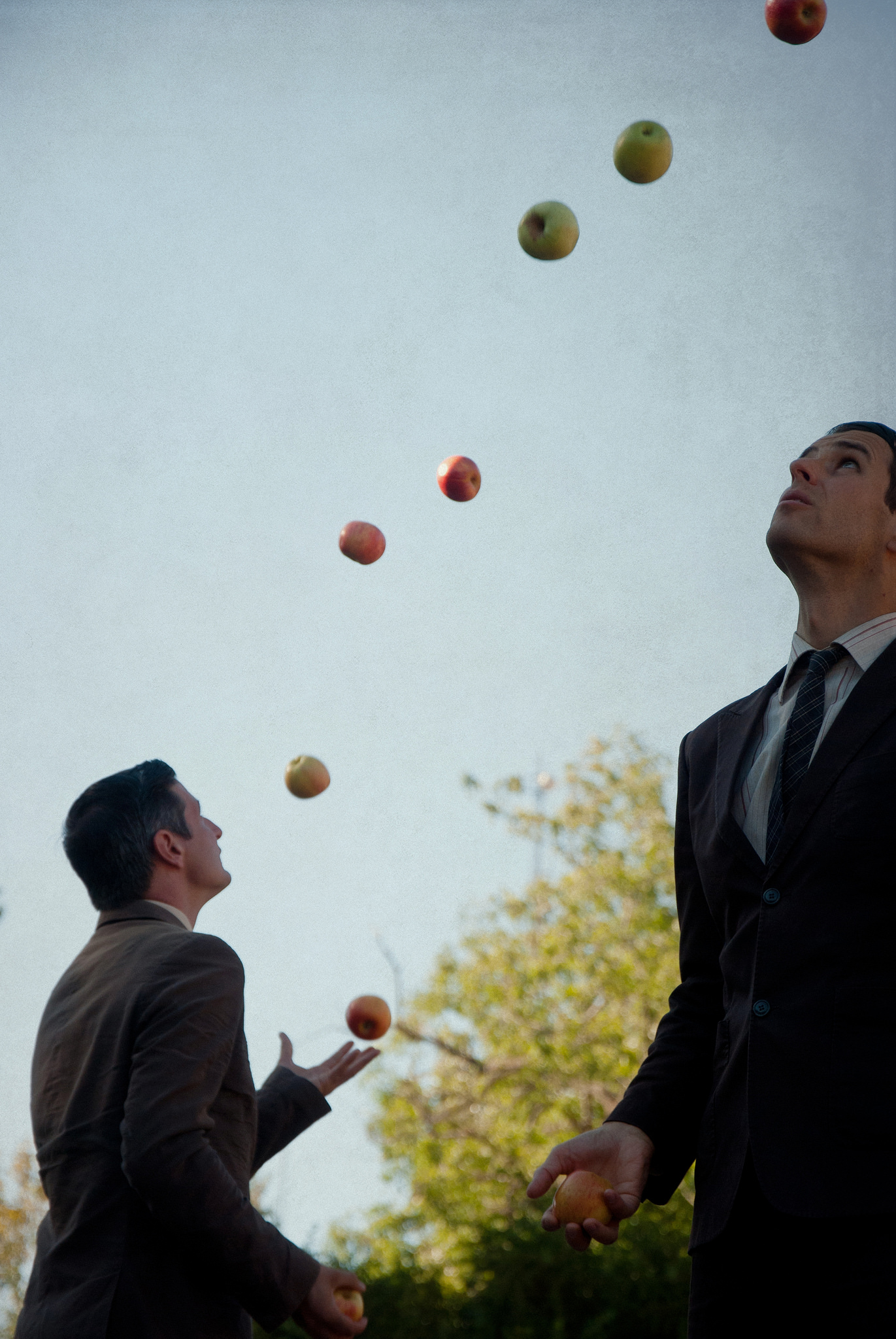 Two men in business suits juggle apples