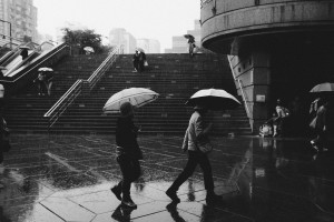 Black-and-white photograph of two people with umbrellas walking in the rain