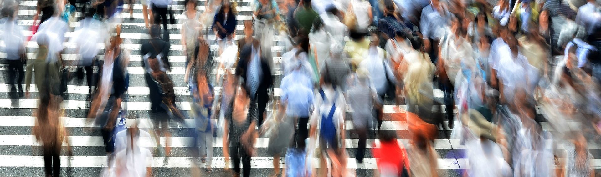 An extended exposure photograph of pedestrians crossing the street. The extended exposure has captured the movement of individuals, show their movement across the street.