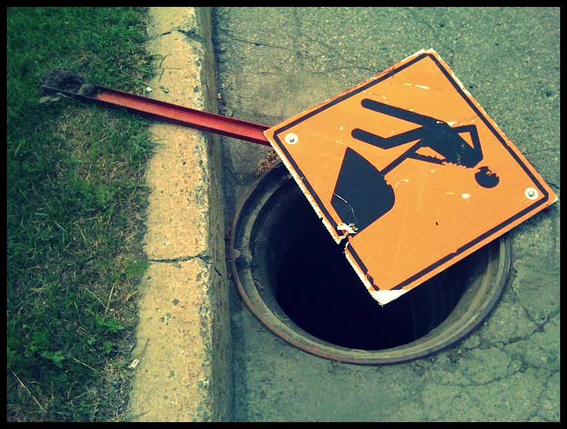 Photo of a hole in street (without its manhole cover), partially covered by a 