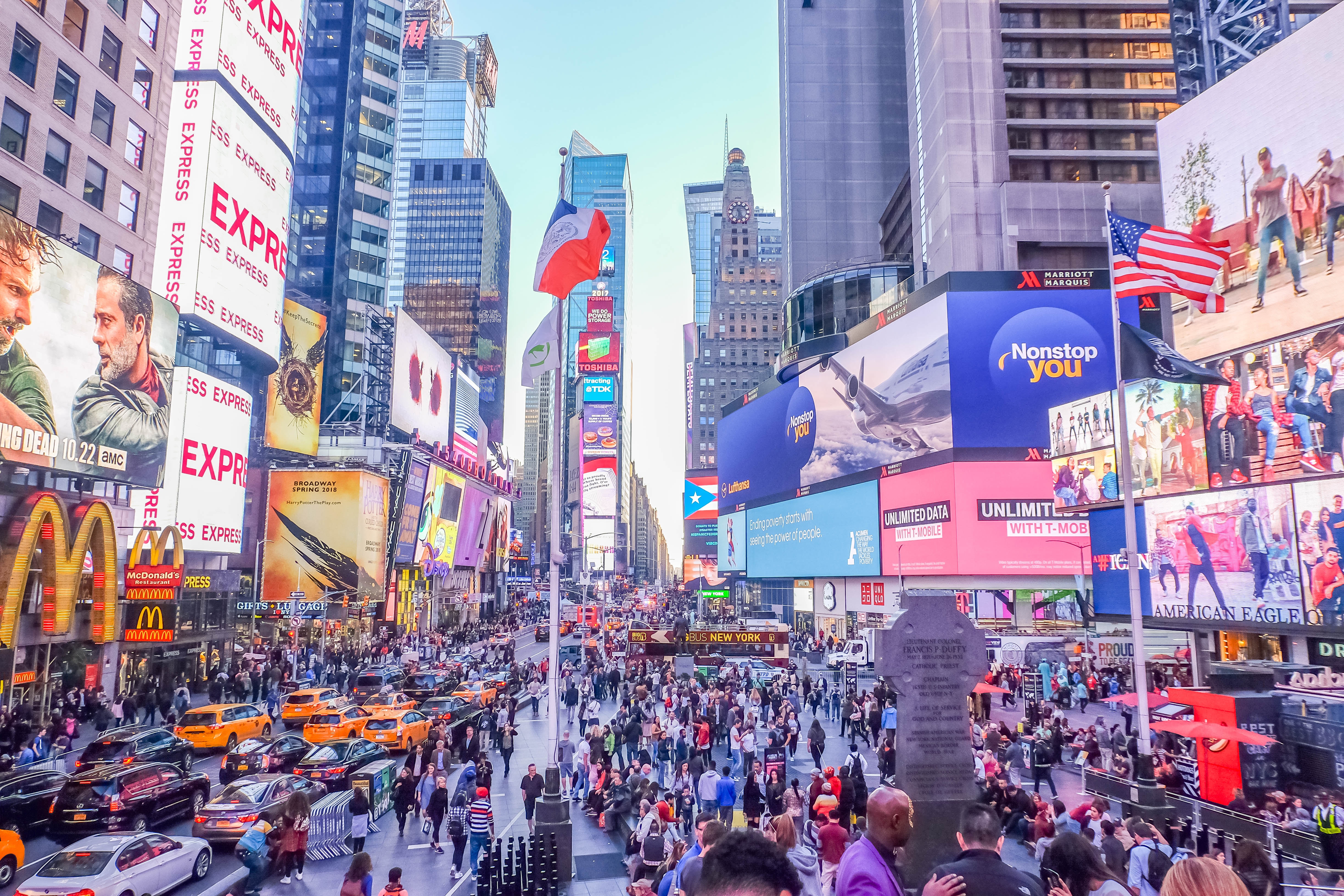 This photo shows Times Square in New York City, NY. The street is crowded with people and yellow taxis in the foreground. 