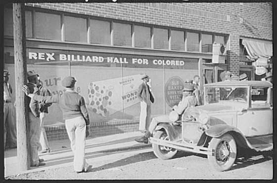 A group of black men and an old car standing outside a billiard hall. The words 