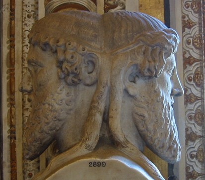 A photo of a statue of Janus. The statue is of two heads facing outwards with the backs of their heads molded together.
