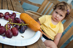 toddler girl sits behind her grapes and hotdog with a grumpy face.