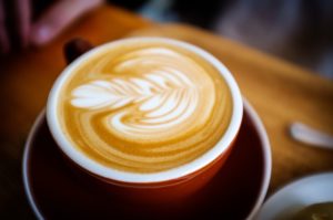 Photo of a cappuccino with a leaf picture artfully drawn in the foam. An example of coffee