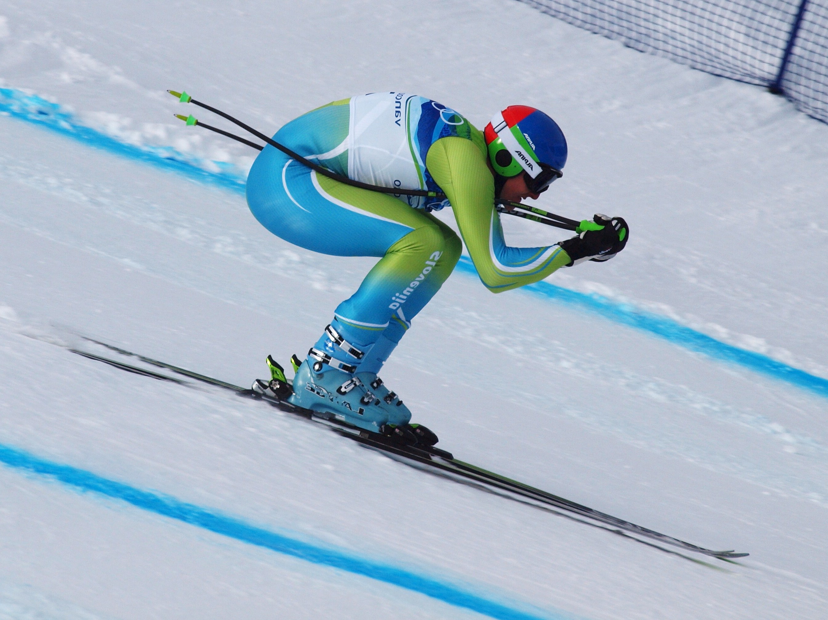 Olympic skier tucked as he races downhill.