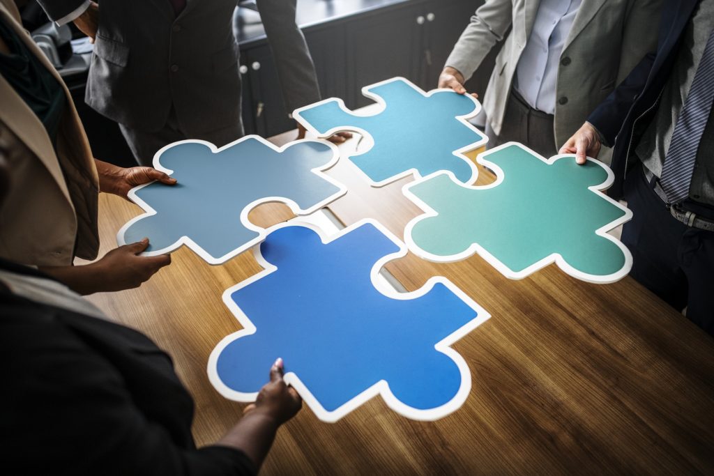 Photograph of four large puzzle pieces being put together. The individuals holding the puzzle pieces are not included in the photo.
