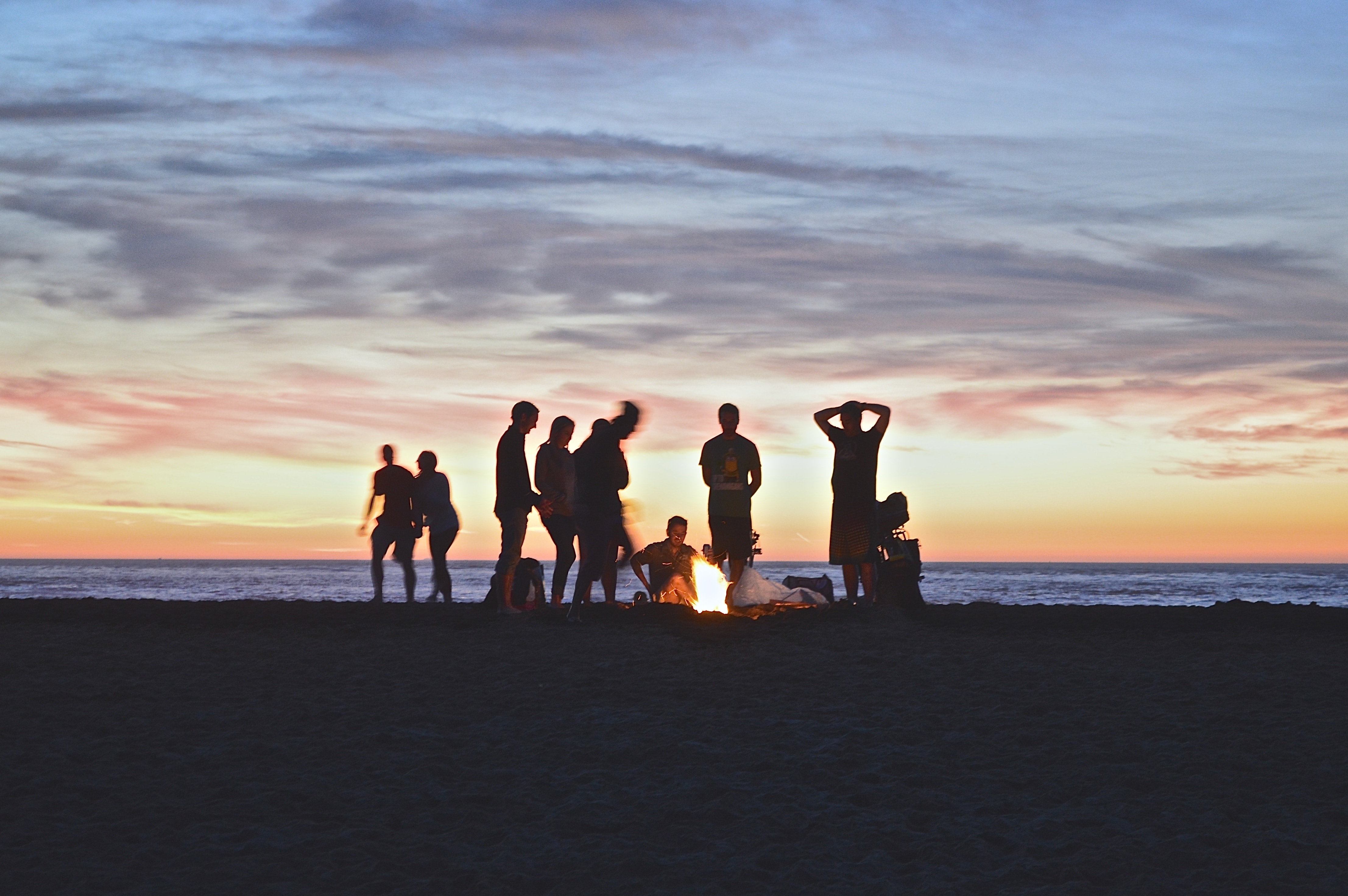 Photograph of several people standing around a fire on a beach.