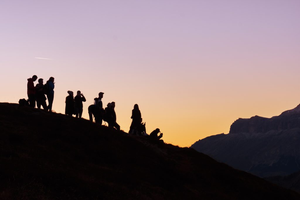 Photograph of several individuals hiking. The sun is setting, casting all individuals in shadow.