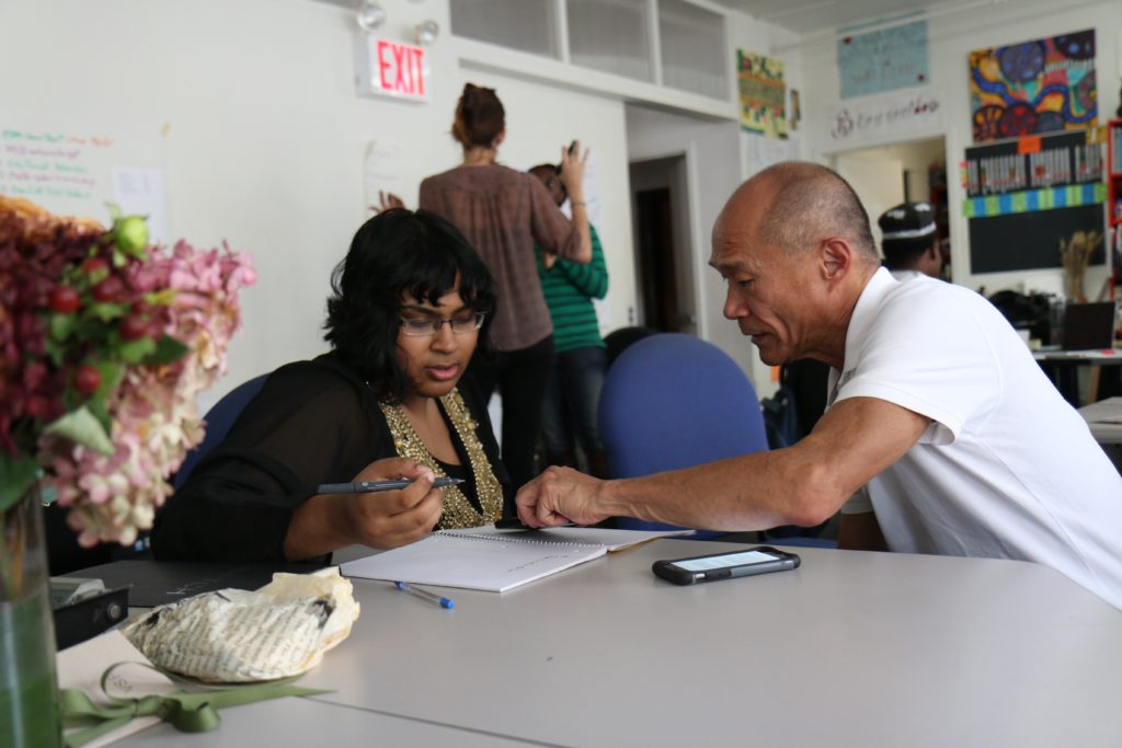 Photograph of an older man helping a young woman fill out paperwork.