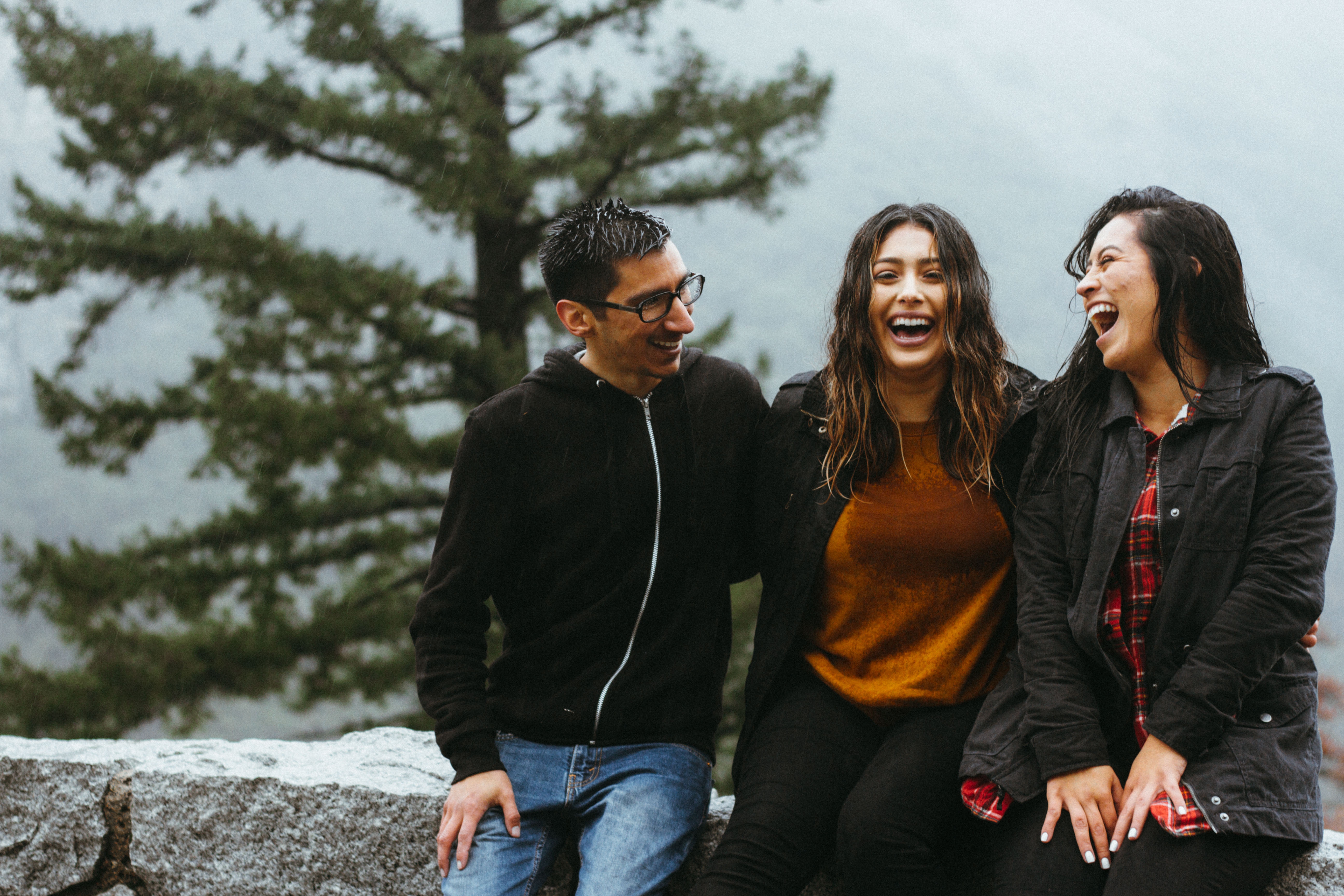 A man and two women sit on a stone wall. The three of them are laughing, enjoying one another's company.