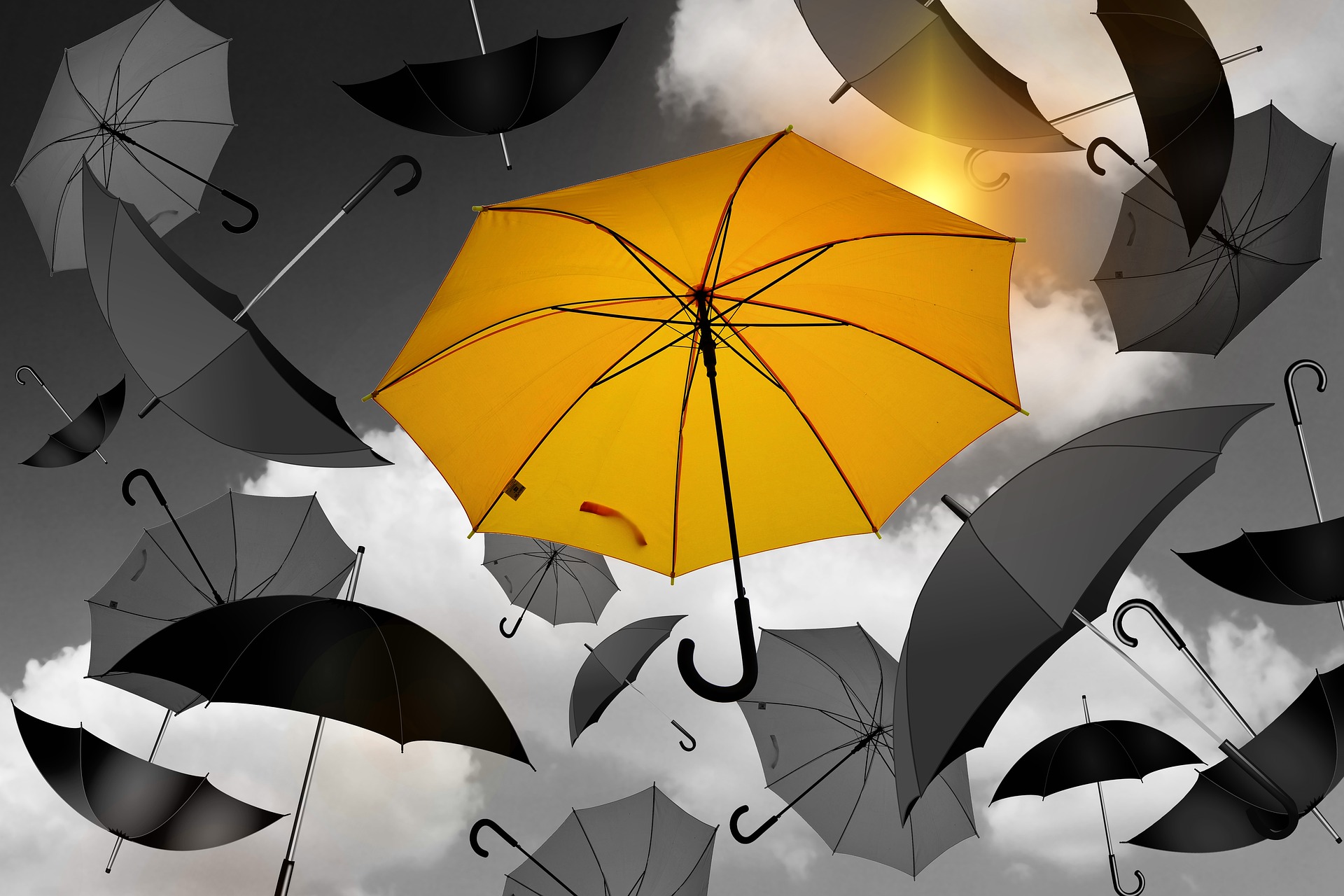 Image of several grey umbrellas floating in the sky. A single yellow umbrella floats in the middle of the picture in front of the grey umbrellas.