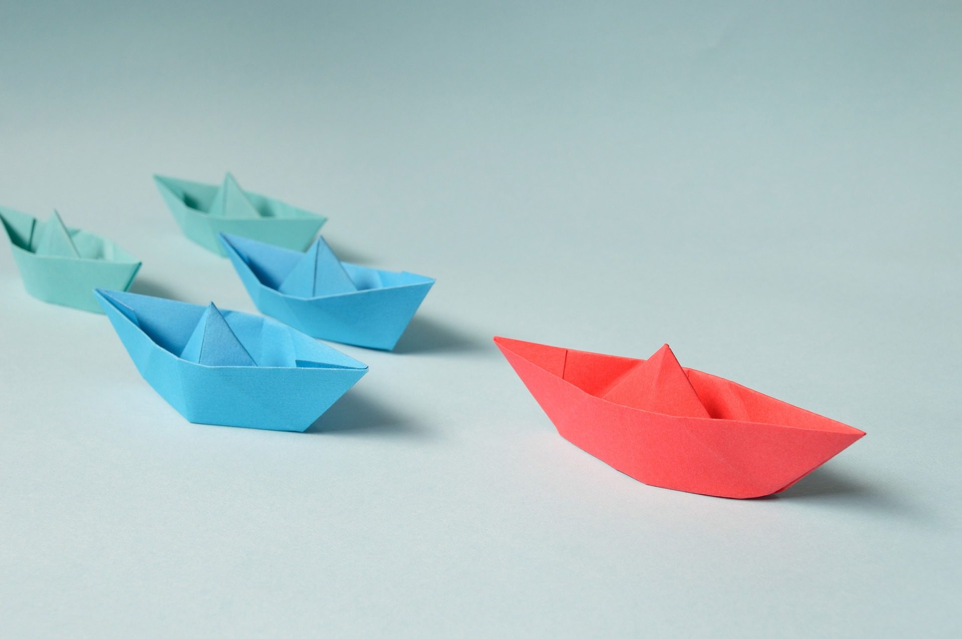 A red origami boat leads several blue boats across the photo