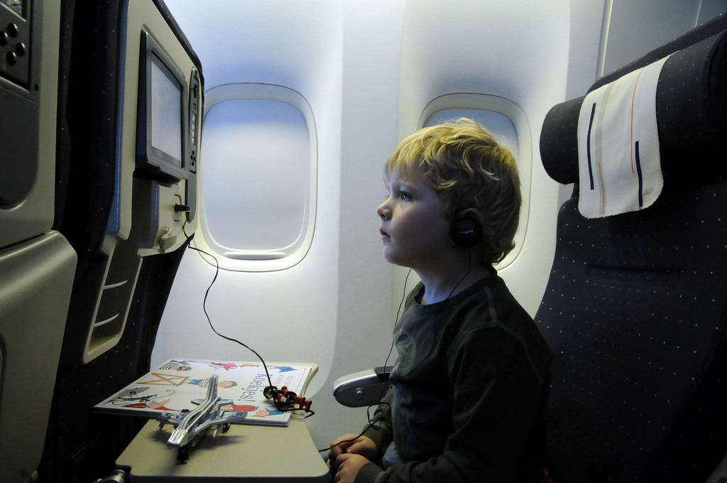 Young boy is shown in profile while seated in an airplane. He's watching something on the video screen in front of him.