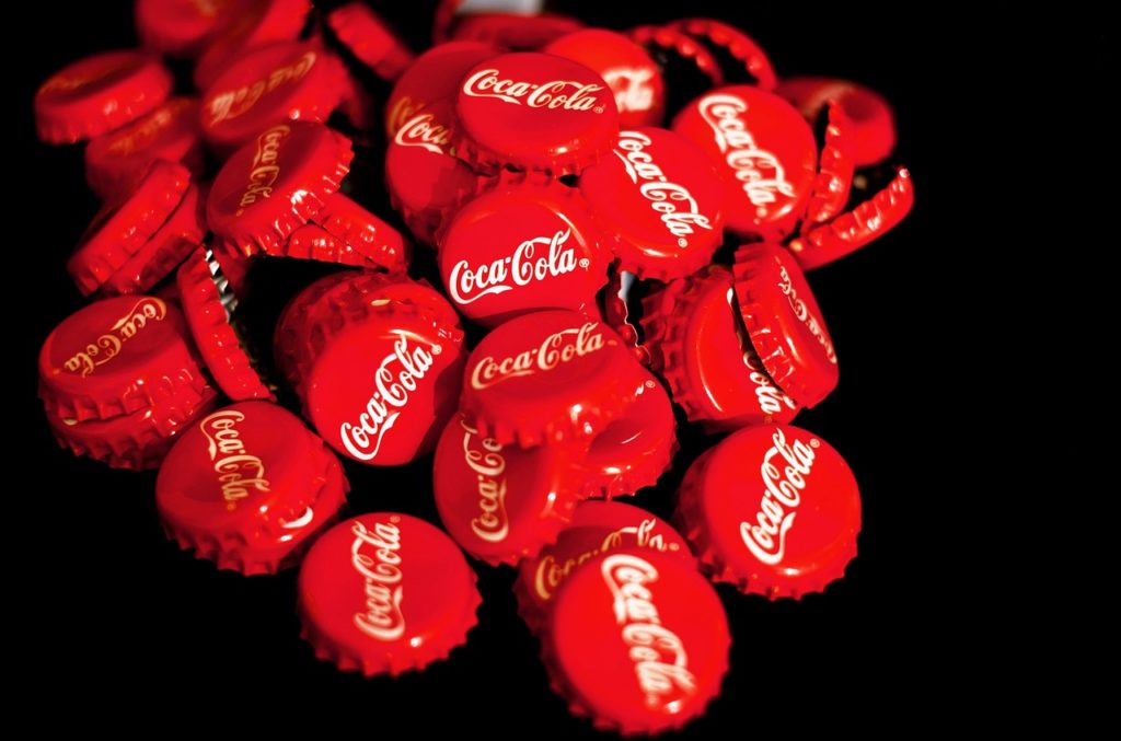 A pile of coca cola bottle caps. They are red and have the name Coca Cola written on each in their customary cursive font