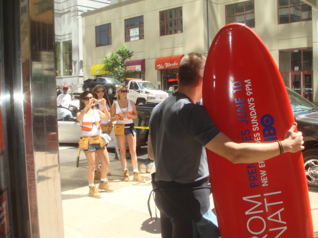 Photograph of a man with a bright red surfboard with an ad for 