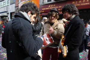Three male hipsters play instruments on a street in Chinatown.