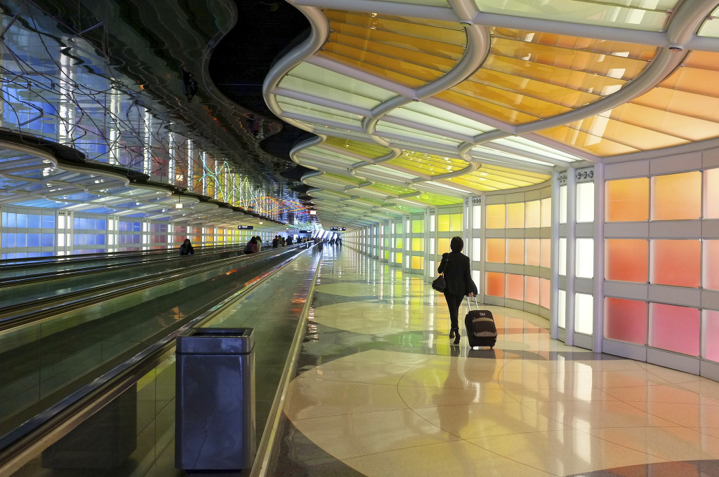Photo of a lone traveler pulling her suitcase, walking through brightly colored O'Hare Airport 