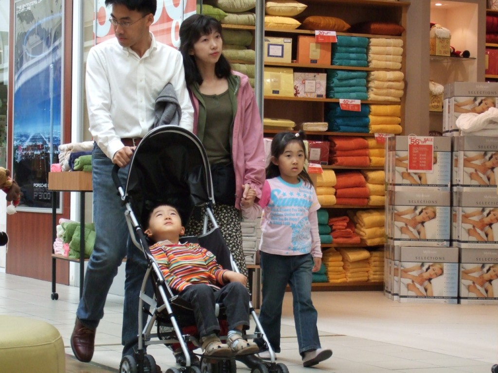 Photo of a family shopping in a household goods store: The father pushes a his young son in the stroller; his wife is next to him, holding the daughter's hand.