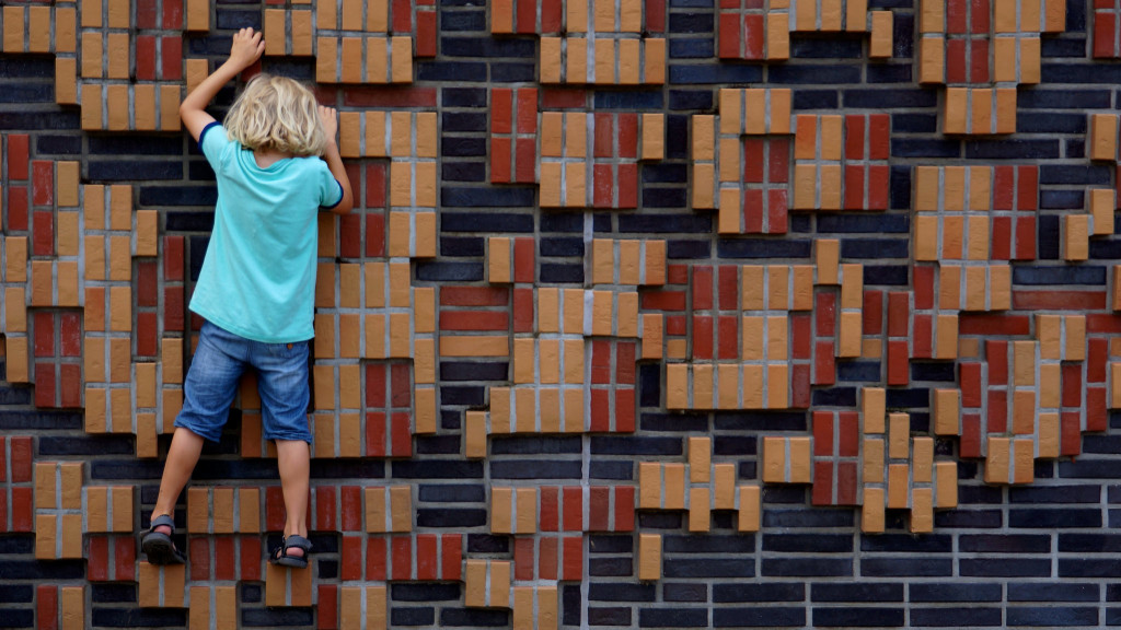Photo of a child climbing a brightly colored brick wall.