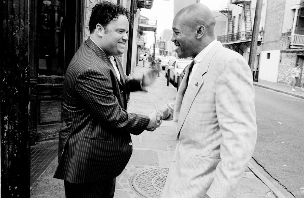 Two men in suits smiling and shaking hands.