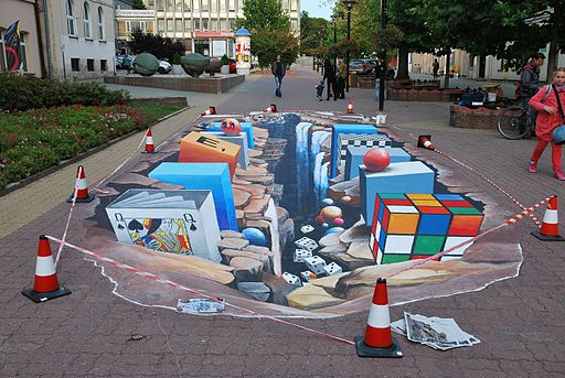 3D street art showing a rubix cube, deck of cards, waterfall, and blocks all on a 2D surface.
