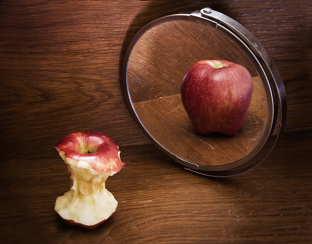 Photo depicting anorexia. A mostly-eaten skinny apply is looking in the mirror and the reflection shows a whole apple.
