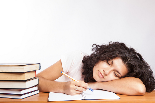 A college students falls asleep on her books while studying.