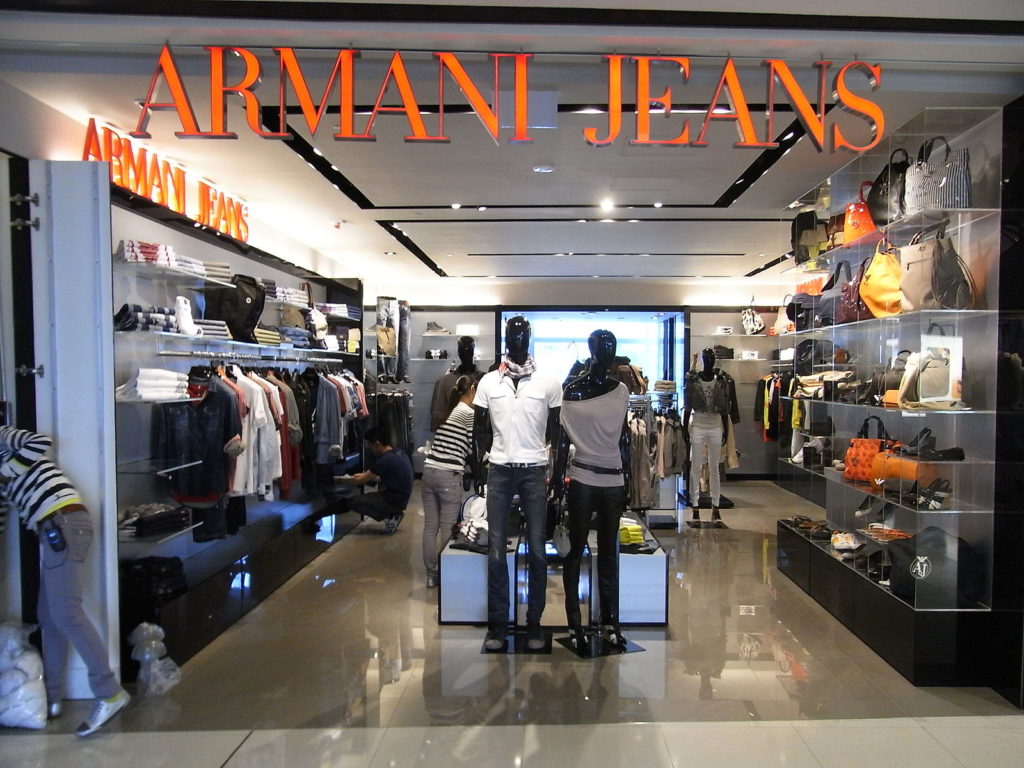 Photograph of an Armani Jeans store. There is merchandise along the exterior walls of the store, and a center shelf with merchandise throughout the middle of the store.