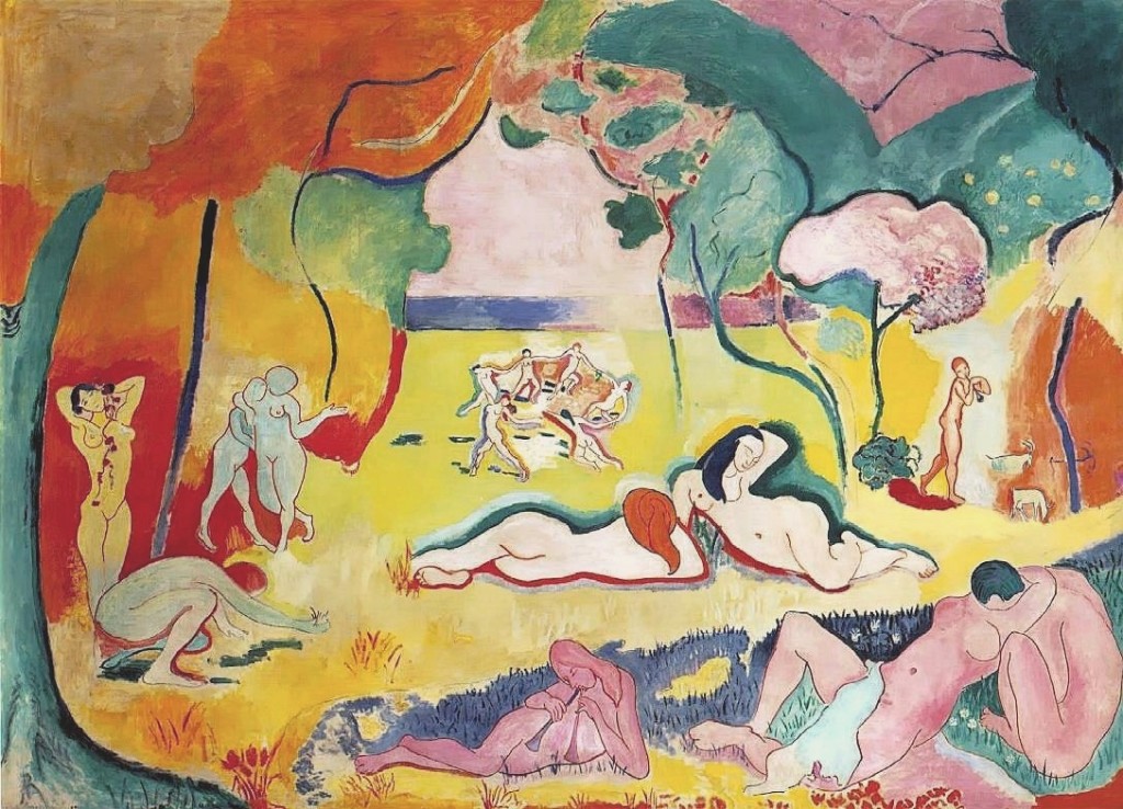 A scene of several nudes relaxing on a grassy field. The scenery around the people is abstract and the trees that line the field blend into one another. The color palette is bright, and not entirely realistic. Some individuals have typical Caucasian coloring, but others are painted in greenish hues, while others are almost purple. In the center of the background, several figures are holding hands in a circle.